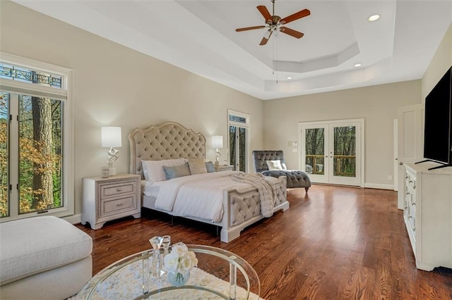 bedroom with dark wood-style flooring, access to exterior, a tray ceiling, french doors, and recessed lighting