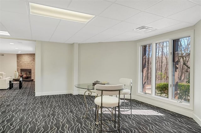 dining space featuring carpet floors, visible vents, a large fireplace, a drop ceiling, and baseboards