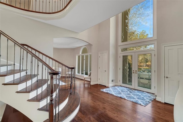 foyer with baseboards, arched walkways, wood finished floors, a high ceiling, and french doors