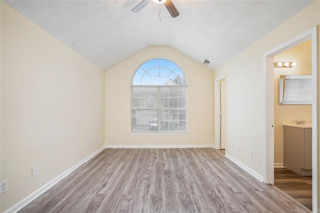 empty room with wood finished floors, a ceiling fan, visible vents, baseboards, and vaulted ceiling