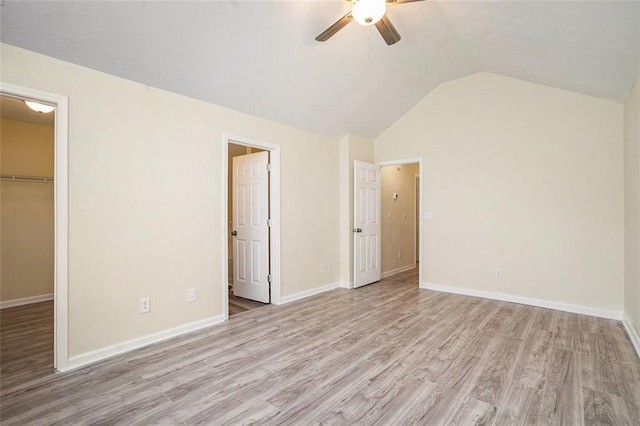 unfurnished bedroom featuring lofted ceiling, a closet, a spacious closet, baseboards, and light wood-style floors