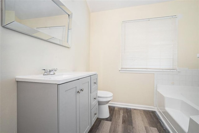 bathroom featuring toilet, baseboards, a bath, vanity, and wood finished floors