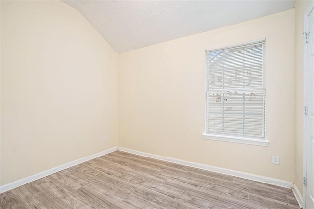 spare room featuring baseboards, light wood-type flooring, and vaulted ceiling