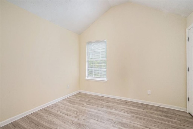 empty room featuring baseboards, light wood-style flooring, and vaulted ceiling