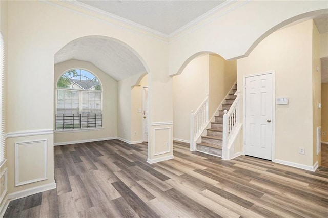 foyer entrance featuring wood finished floors, ornamental molding, stairway, vaulted ceiling, and baseboards