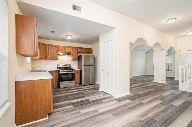 kitchen with under cabinet range hood, visible vents, a sink, wood finished floors, and stainless steel appliances
