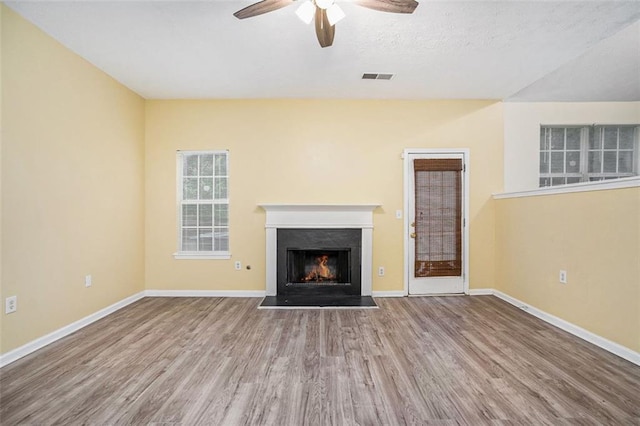 unfurnished living room featuring wood finished floors, visible vents, baseboards, ceiling fan, and a warm lit fireplace