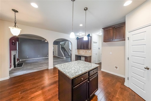 kitchen featuring dark brown cabinetry, a center island, hanging light fixtures, dark hardwood / wood-style floors, and light stone countertops