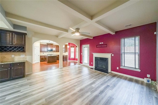 unfurnished living room featuring ceiling fan, a fireplace, light hardwood / wood-style floors, and beamed ceiling