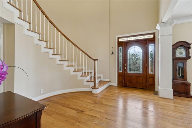 foyer with light wood finished floors, baseboards, stairs, decorative columns, and a towering ceiling