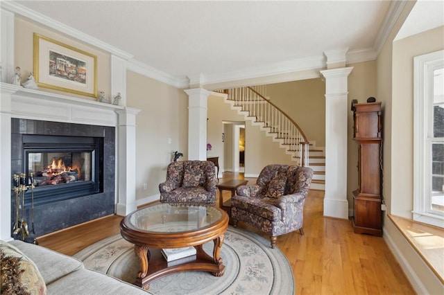 living room featuring stairway, ornate columns, a fireplace, ornamental molding, and light wood-style floors