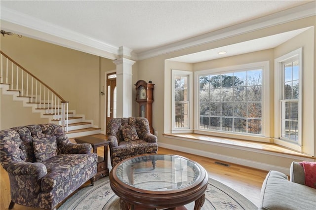 living area with visible vents, crown molding, stairway, decorative columns, and wood finished floors