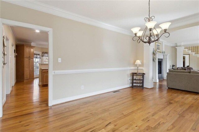 unfurnished living room with a notable chandelier, a fireplace, light wood-type flooring, and crown molding