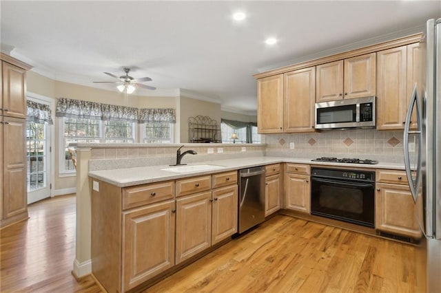 kitchen with tasteful backsplash, light countertops, appliances with stainless steel finishes, a peninsula, and a sink