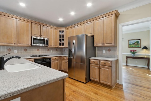 kitchen with a sink, stainless steel appliances, light wood-style floors, crown molding, and glass insert cabinets