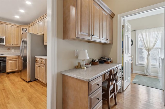 kitchen with black appliances, light countertops, built in desk, and light wood finished floors