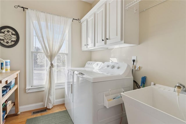 clothes washing area with visible vents, a sink, cabinet space, light wood finished floors, and washing machine and clothes dryer