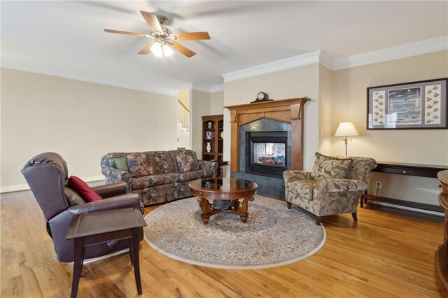 living room with a ceiling fan, crown molding, wood finished floors, and a premium fireplace