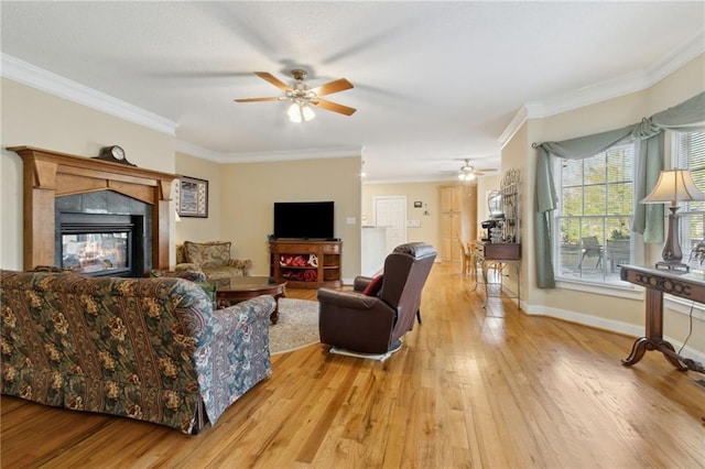 living room with baseboards, light wood-style flooring, ceiling fan, a tile fireplace, and ornamental molding