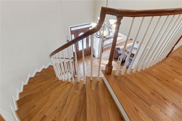 stairway with baseboards, a notable chandelier, and wood finished floors