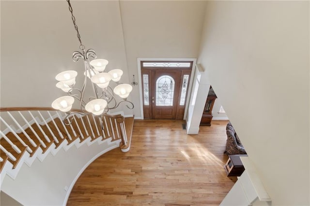 entryway featuring baseboards, stairway, light wood-type flooring, a towering ceiling, and a notable chandelier