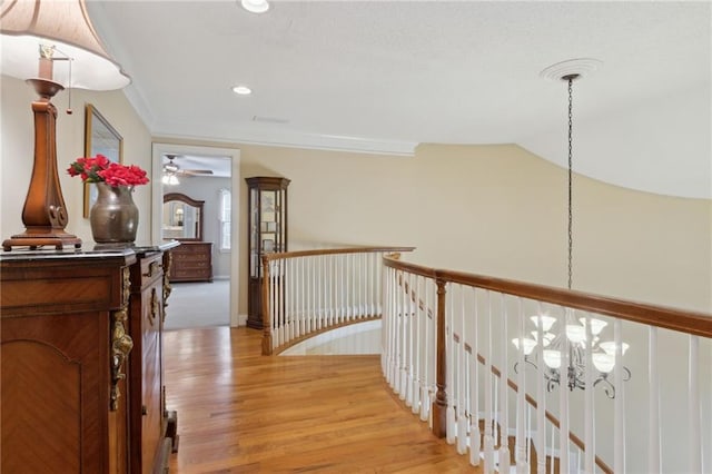 corridor featuring light wood finished floors, ornamental molding, vaulted ceiling, a notable chandelier, and an upstairs landing