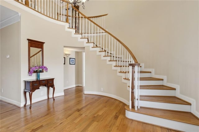 stairs featuring a high ceiling, a notable chandelier, wood finished floors, and baseboards