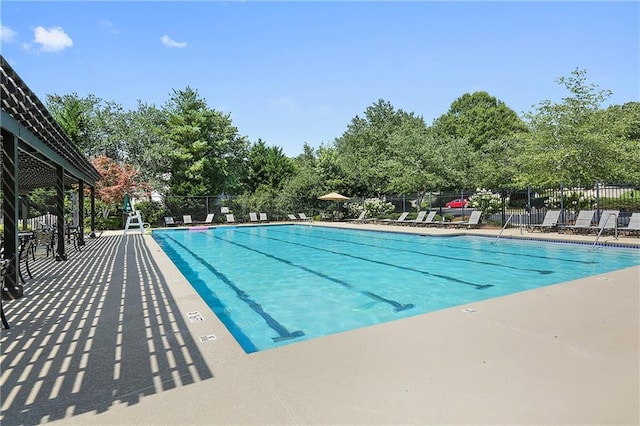 community pool featuring fence, view of wooded area, and a patio area
