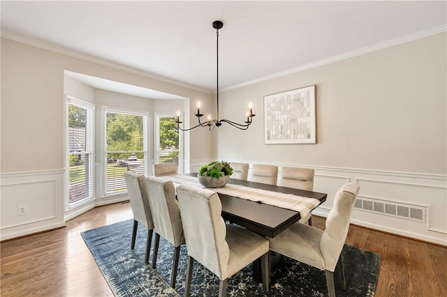 dining space with a chandelier, wood finished floors, crown molding, a wainscoted wall, and a decorative wall