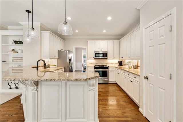 kitchen featuring stainless steel appliances, a sink, a peninsula, ornamental molding, and light stone countertops