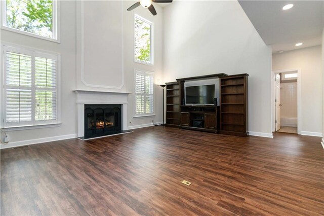 5073 Kingsbridge Pass, Powder Springs, GA 30127 - unfurnished living room featuring a ceiling fan, a lit fireplace, a towering ceiling, baseboards, and dark wood-style floors