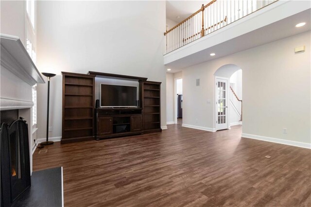 5073 Kingsbridge Pass, Powder Springs, GA 30127 - unfurnished living room featuring dark wood finished floors, stairway, a fireplace with raised hearth, a high ceiling, and arched walkways