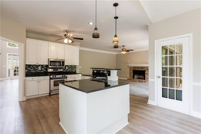 kitchen featuring white cabinetry, appliances with stainless steel finishes, ceiling fan, dark countertops, and a stone fireplace
