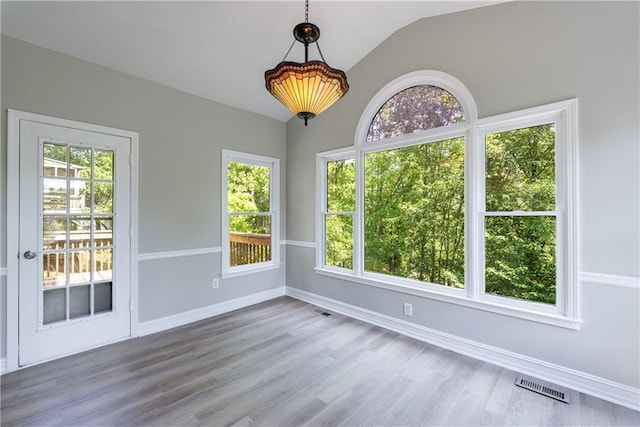 unfurnished room with visible vents, wood finished floors, vaulted ceiling, and plenty of natural light