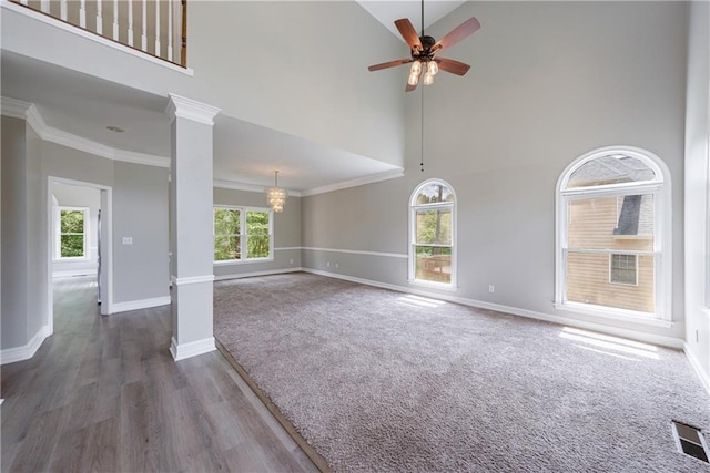 unfurnished living room featuring ornamental molding, ceiling fan with notable chandelier, baseboards, visible vents, and a towering ceiling