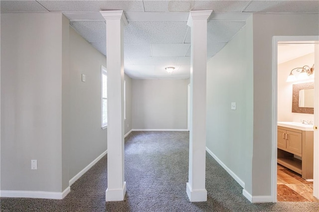 basement featuring a sink, a drop ceiling, baseboards, and carpet floors