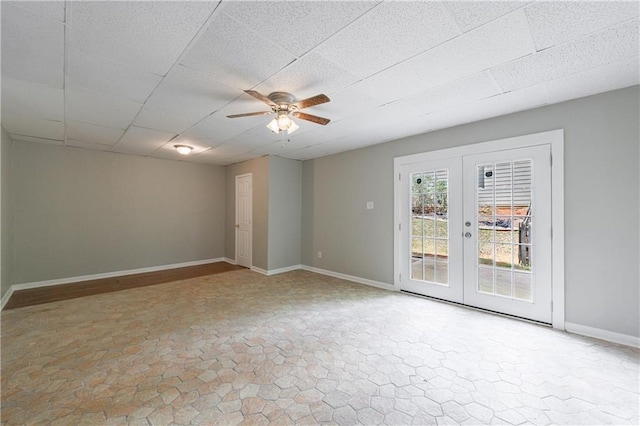 empty room with a drop ceiling, stone finish floor, ceiling fan, baseboards, and french doors