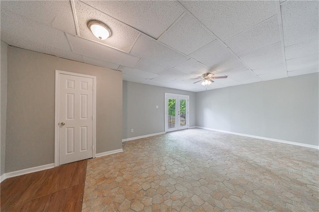 empty room featuring stone finish floor, ceiling fan, a paneled ceiling, and baseboards