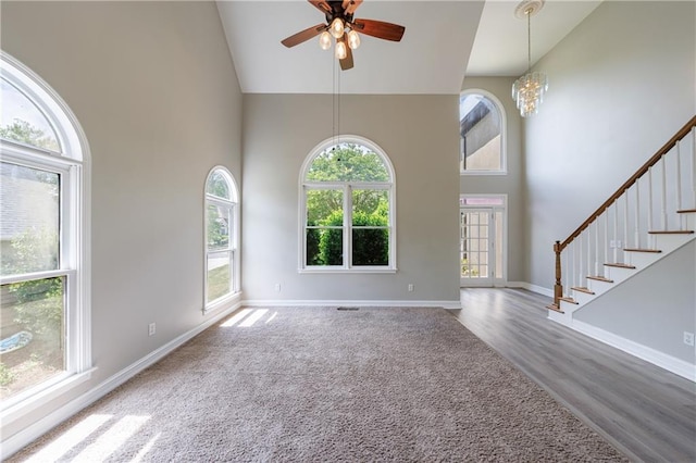 unfurnished living room featuring stairway, high vaulted ceiling, ceiling fan with notable chandelier, and baseboards