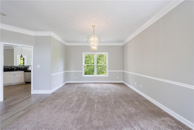 spare room featuring carpet, a chandelier, ornamental molding, and baseboards