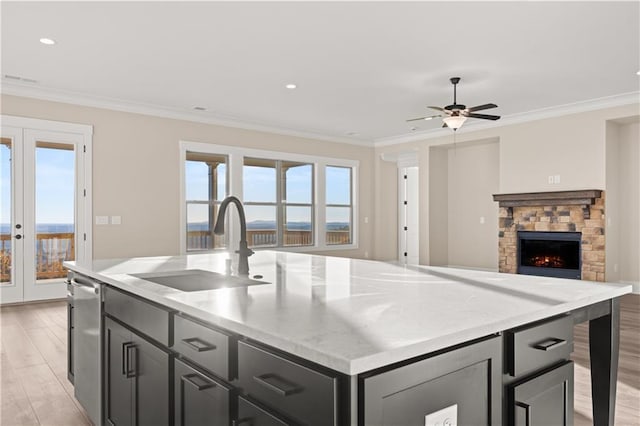 kitchen with a fireplace, an island with sink, sink, ceiling fan, and crown molding