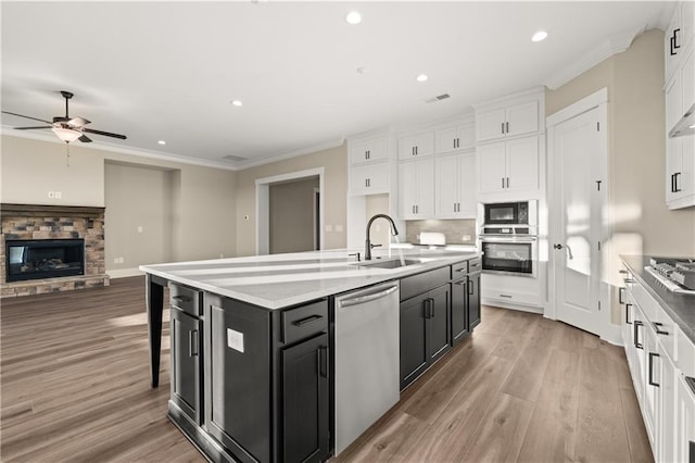 kitchen with a center island with sink, sink, a stone fireplace, stainless steel appliances, and white cabinets