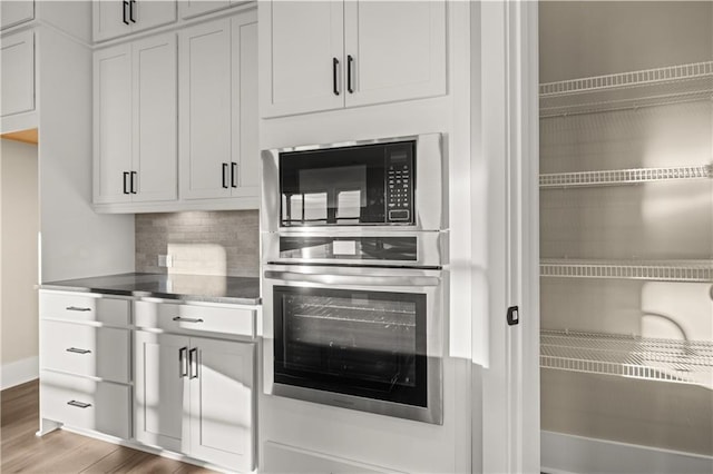 kitchen with hardwood / wood-style floors, decorative backsplash, stainless steel oven, black microwave, and white cabinets