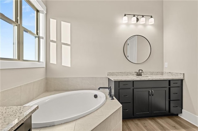 bathroom with tiled bath, hardwood / wood-style flooring, and vanity