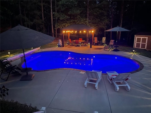 pool at twilight with a fenced in pool, an outbuilding, a shed, and a patio area