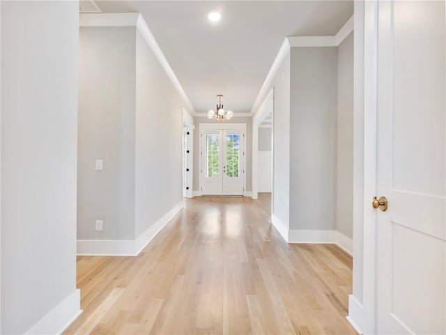 entrance foyer featuring an inviting chandelier, ornamental molding, french doors, and light wood-type flooring