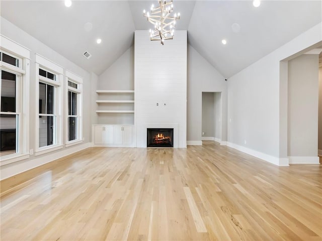 unfurnished living room featuring light hardwood / wood-style flooring, high vaulted ceiling, a fireplace, built in shelves, and a chandelier