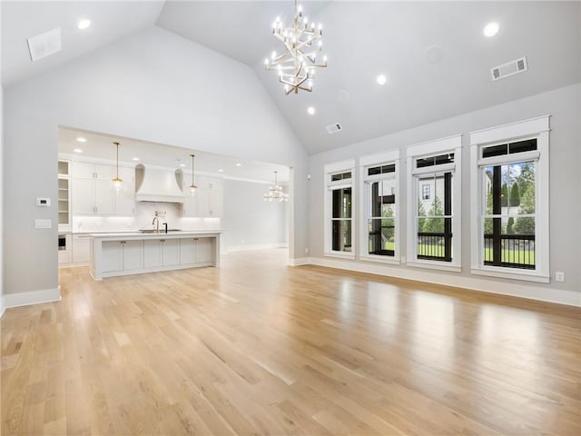 unfurnished living room with high vaulted ceiling, sink, a notable chandelier, and light wood-type flooring