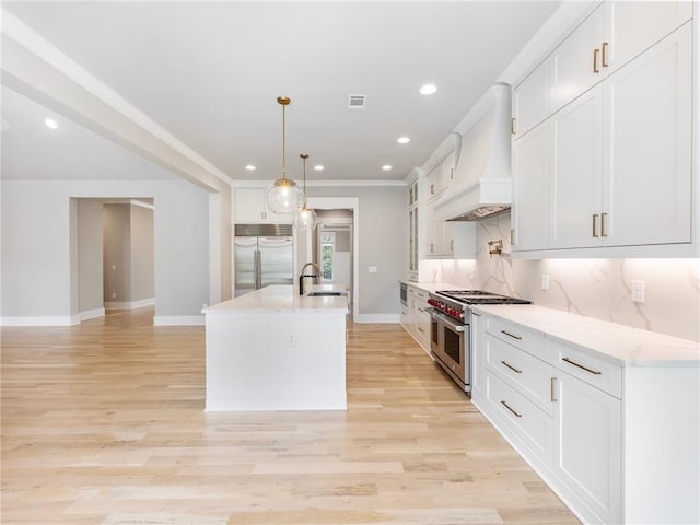 kitchen with high end appliances, white cabinetry, custom exhaust hood, and an island with sink