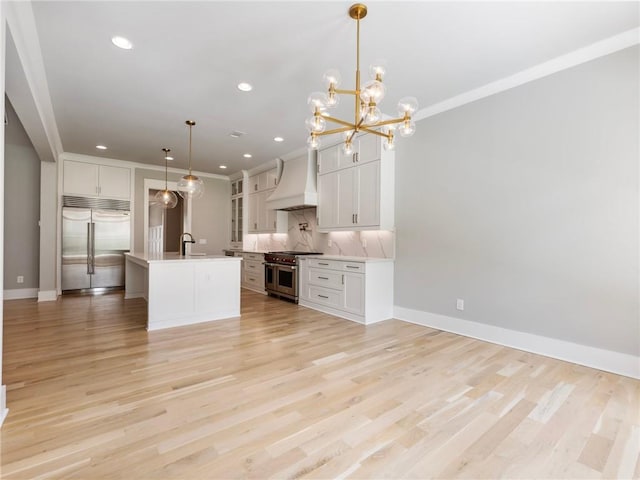 kitchen with decorative light fixtures, white cabinetry, custom exhaust hood, high end appliances, and a kitchen island with sink